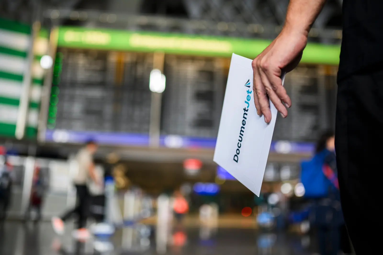 Courier holding a DocumentJet document envelope in front of an airport departure board